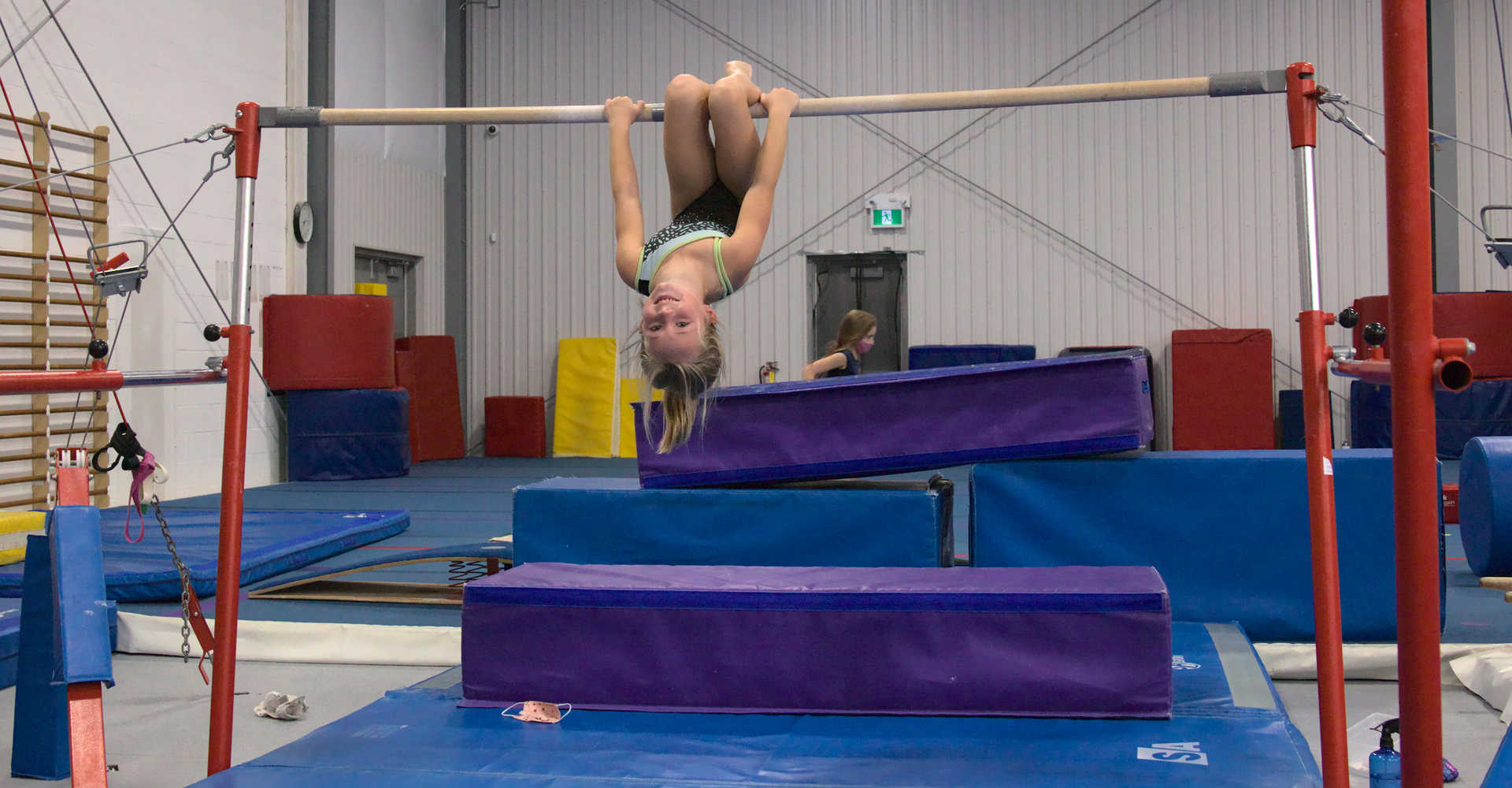 A smiling young gymnast on the bar taking a small break to catch a breath at Gymworld Adventures in Gymnastics