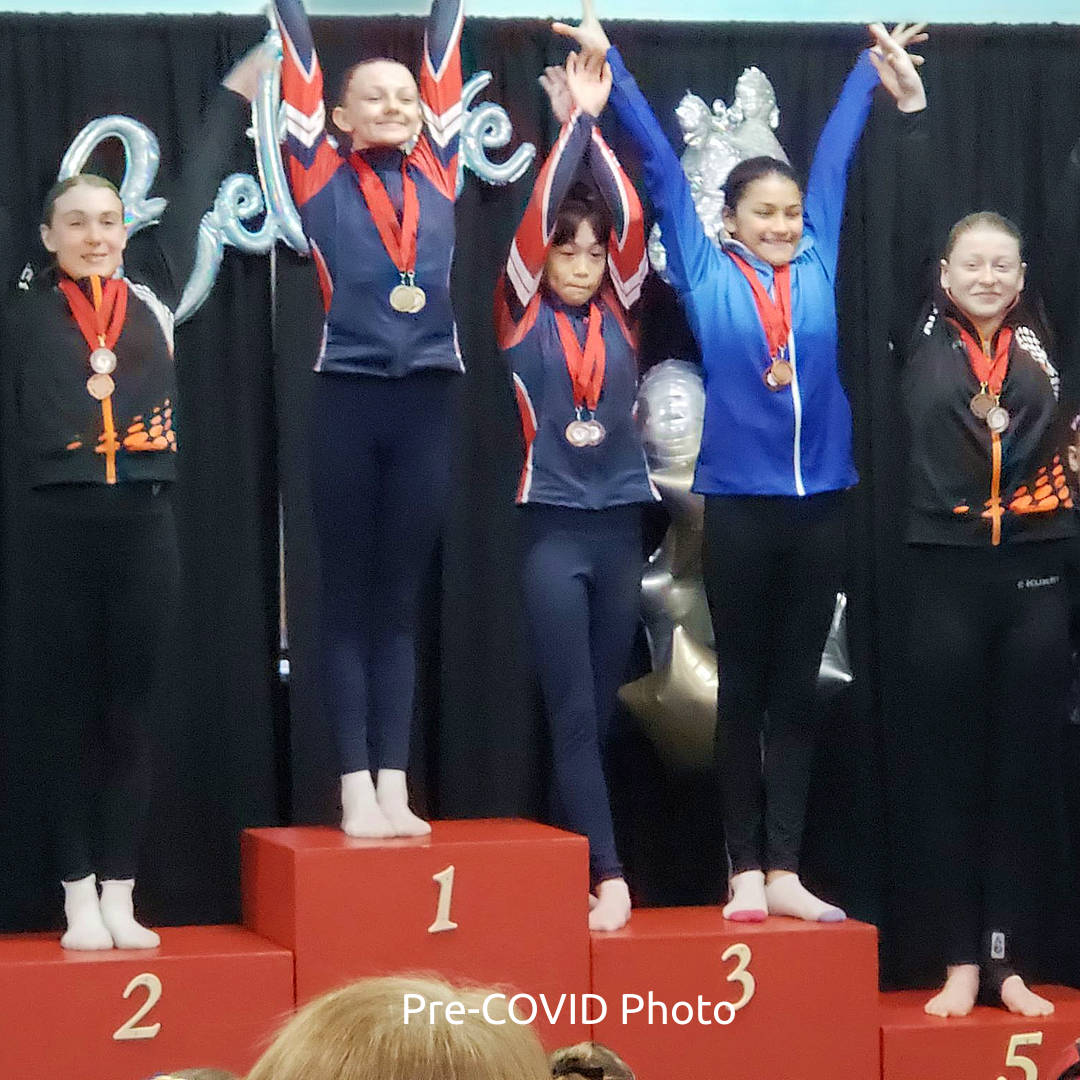 GW Elites gymnast with other gymnasts on a podium, medals and all, at a competion.